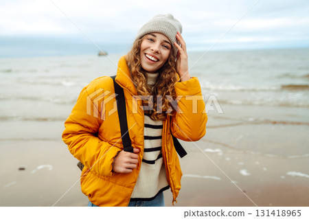 A beautiful young tourist woman in a yellow jacket with a backpack enjoys life near the sea. Travel. 131418965
