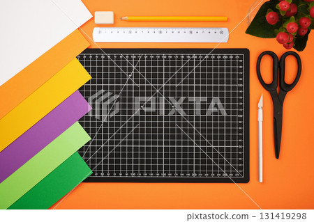 Colorful paper sheets, cutting mat, scissors, ruler, pencil, knife, and eraser on orange background. Desktop for paper crafts. Colorful paper sheets, cutting mat, scissors, ruler, pencil, knife, and eraser on orange background. Desktop for paper crafts. 131419298