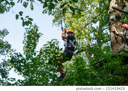 Man riding zipline through green forest in adventure park Man riding zipline through green forest in adventure park 131419428