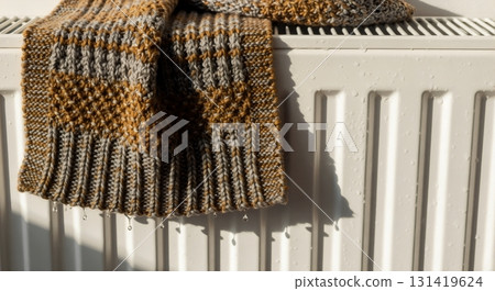 Wet knitted scarf drying on a white radiator. Water droplets visible on fabric and metal surface. Home heating and winter comfort concept 131419624