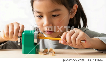 Young Asian girl sharpening a yellow pencil with a manual sharpener. Focused child preparing school supplies at a desk. Back to school and education concept 131419662