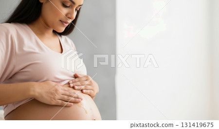 Pregnant woman rubbing oil on her belly. Maternity skin care and self-care routine. Expectant mother moisturizing abdomen with copy space 131419675