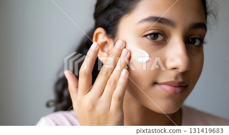 Young Middle Eastern woman applying moisturizer to her face. Close up of her daily skincare routine. Healthy skin and beauty concept Young Middle Eastern woman applying moisturizer to her face. Close up of her daily skincare routine. Healthy skin and beauty concept 131419683