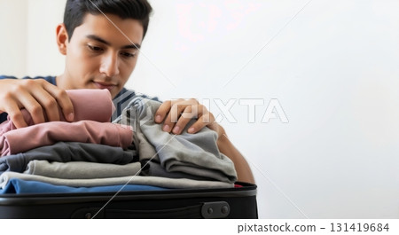 Young Hispanic man packing clothes into a suitcase. Travel preparation and organization for a dorm room. Copy space Young Hispanic man packing clothes into a suitcase. Travel preparation and organization for a dorm room. Copy space 131419684