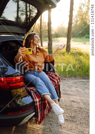 Happy Woman is resting in trunk of car and taking selfie. Selfie time. Lifestyle, travel 131419748
