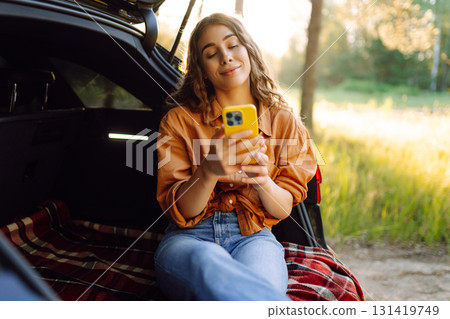 Young woman enjoys a sunny day outdoors while sitting in her car. Travel, weekend, nature, relax 131419749
