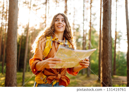 A traveler woman stands in a lush forest, examining a map with a focused expression 131419761