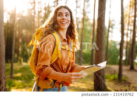 A traveler woman stands in a lush forest, examining a map with a focused expression 131419762