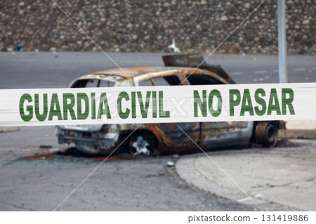 Spanish police tape in front of a burnt car 131419886