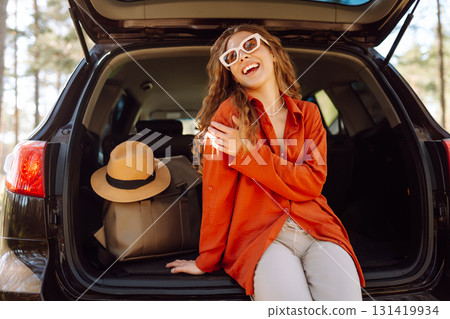 Happy woman enjoying nature while sitting in the trunk of her car during a solo trip. Road trip 131419934