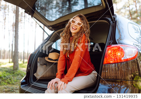 Happy woman enjoying nature while sitting in the trunk of her car during a solo trip. Road trip Happy woman enjoying nature while sitting in the trunk of her car during a solo trip. Road trip 131419935
