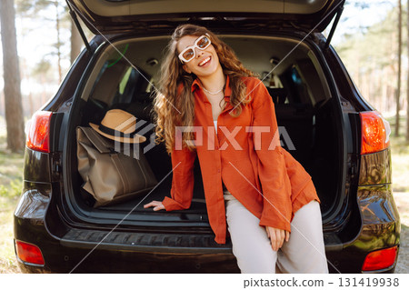 Happy woman enjoying nature while sitting in the trunk of her car during a solo trip. Road trip Happy woman enjoying nature while sitting in the trunk of her car during a solo trip. Road trip 131419938