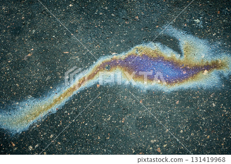 Polluting oil stain on dark asphalt creating iridescent rainbow colors, showing environmental issue 131419968