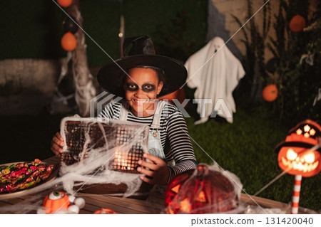 Girl wearing witch costume holding spooky Halloween lantern during a masquerade ball 131420040