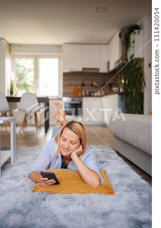 Woman relaxing on the floor using her smartphone at home 131420054