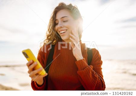 Young woman using mobile phone at beach. Cold weather. Autumn. Blogging, communication 131420192