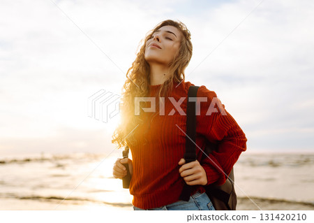 As she walked along the beach, the woman tourist adjusted her backpack, taking in the salty sea air As she walked along the beach, the woman tourist adjusted her backpack, taking in the salty sea air 131420210