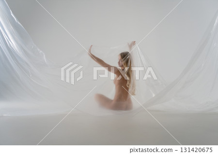 Blonde woman poses gracefully with sheer fabric in a studio setting 131420675
