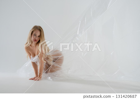 Blonde woman in a beauty studio poses gracefully with transparent fabric 131420687