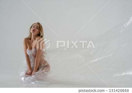 Woman with blonde hair poses in a beauty studio setting wrapped in plastic 131420688