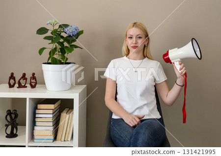 Confident young woman with megaphone sitting indoors 131421995