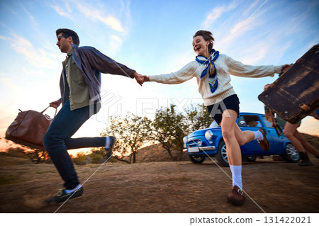 Happy couple holding hands and running with suitcases by retro blue car 131422021
