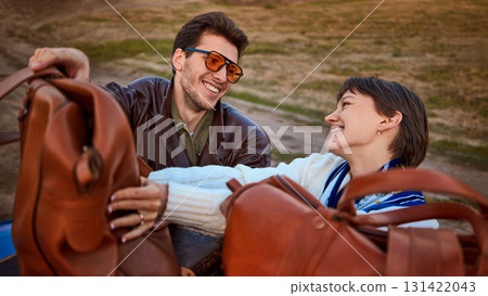 Happy couple unpacking leather bags from blue retro car roof during trip 131422043