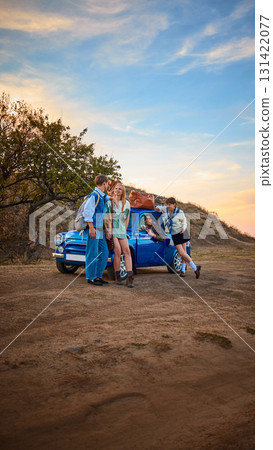 Young travelers with retro car on countryside road during golden sunset Young travelers with retro car on countryside road during golden sunset 131422077