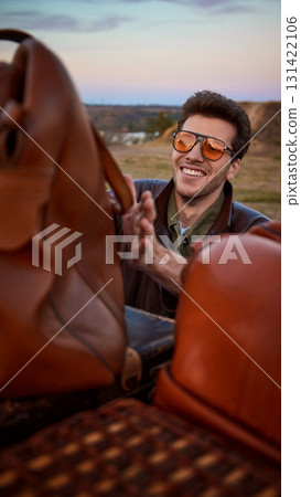 Man with sunglasses smiling while loading vintage travel bags on retro car Man with sunglasses smiling while loading vintage travel bags on retro car 131422106
