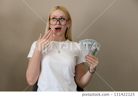Surprised woman holding fan of dollar bills in casual setting 131422125