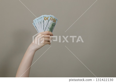 Hand holding fan of hundred dollar bills on neutral Hand holding fan of hundred dollar bills on neutral 131422130