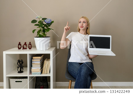 Woman holding laptop with blank screen and pointing up with idea expression Woman holding laptop with blank screen and pointing up with idea expression 131422249