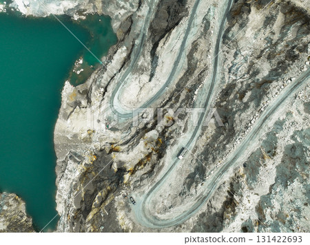 Aerial view of a transport truck hauling raw limestone through an open pit quarry, showing industrial mining operations and the environmental impact of material supply for global construction demand. Aerial view of a transport truck hauling raw limestone through an open pit quarry, showing industrial mining operations and the environmental impact of material supply for global construction demand. 131422693