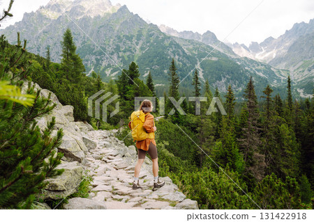 Smiling traveler with a bright backpack on a hiking mountain trail. Active lifestyle. 131422918