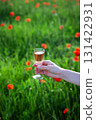 A hand holds a glass of rose wine against a blurred background of a poppy field 131422931