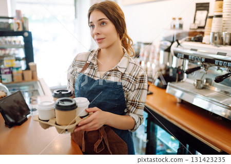 Portrait of a young woman barista holding takeaway coffee in hands. Takeaway food. Business concept. Portrait of a young woman barista holding takeaway coffee in hands. Takeaway food. Business concept. 131423235