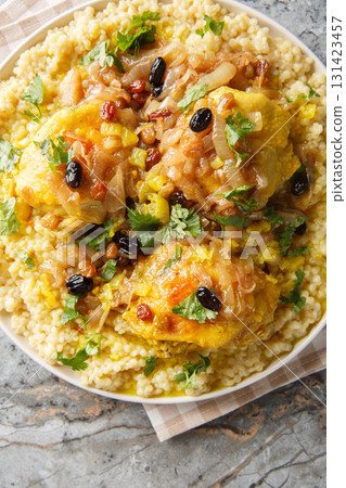 Chicken and Tfaya Couscous is a classic Moroccan dish in which tender couscous is topped with braised chicken and caramelized onion and raisin sauce closeup. Vertical top view 131423457