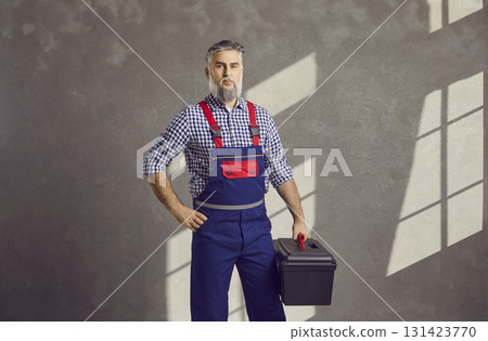 Portrait of senior male worker with toolbox standing on grey wall background at home Portrait of senior male worker with toolbox standing on grey wall background at home 131423770