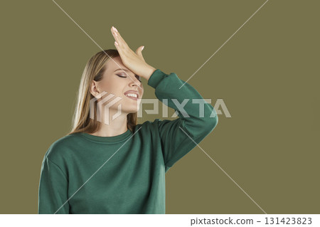 Disappointed embarrassed confused smiling woman with facepalm gesture on khaki background. Disappointed embarrassed confused smiling woman with facepalm gesture on khaki background. 131423823