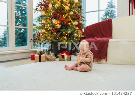 Merry Christmas Xmas. Happy newborn baby child crawling near Christmas tree in living room at home. Little girl kid smiling in room with Christmas decorations. Happy baby in first Christmas eve 131424227