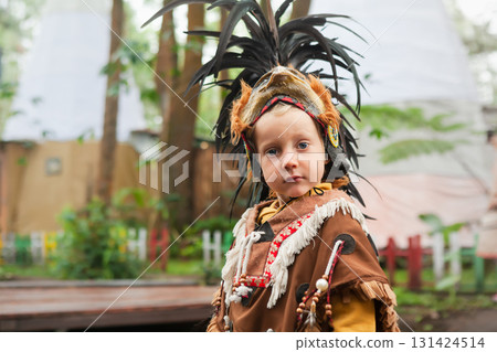 Portrait of a young boy wearing a traditional Indian feathered costume. The image was taken outdoors in a forest like setting, evoking a cultural or educational experience for children. Portrait of a young boy wearing a traditional Indian feathered costume. The image was taken outdoors in a forest like setting, evoking a cultural or educational experience for children. 131424514