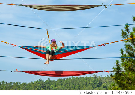 Young woman relaxing in hammock high above ground. A unique high-altitude attraction in Indonesia offering thrilling experiences and panoramic tropical forest views for adventure. Travel on vacation. 131424599