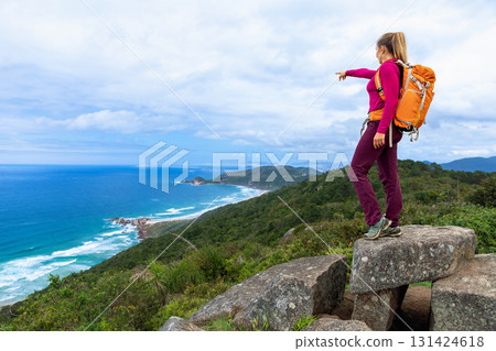 Sporty woman hikes coastal mountain trail with backpack view Sporty woman hikes coastal mountain trail with backpack view 131424618
