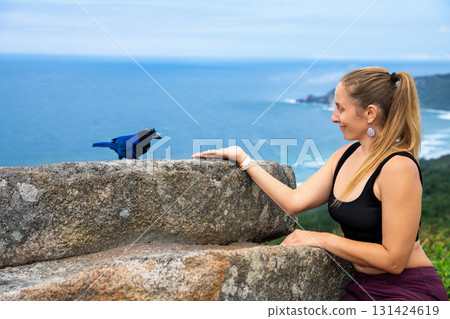 Woman meets bird on cliff with ocean view, travel vibe 131424619