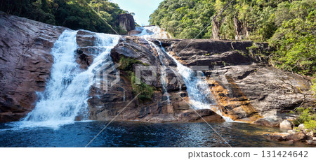 Wide natural waterfall cascading over rocks into blue pool surrounded by lush Atlantic rainforest. Tropical scene from Brazil, Santa Catarina captures untouched beauty and serenity of jungle waterfall 131424642