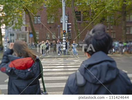 Selective focus. A group of people stand at a crosswalk waiting for the traffic light to turn green in a European city.  131424644