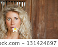 Young blonde woman with frangipani flower on open-air veranda of wooden bungalow in tropical garden. Girl relaxing in luxury villa on family summer vacation. Beach travel, spa, natural lifestyle. 131424697