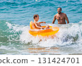 Happy kid with father have fun in sea surf on beach. Joyful child on inflatable ring ride on breaking wave. Travel lifestyle, swimming activities in family summer camp. Vacations on tropical island 131424701