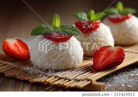White mochi covered in coconut flakes and garnished with strawberries. Mochi with mint on a bamboo mat. 131424913
