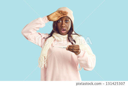 Portrait of sick shocked African American girl in warm winter clothes holding thermometer Portrait of sick shocked African American girl in warm winter clothes holding thermometer 131425307